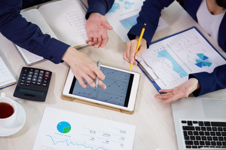 Close-up of business team analyzing graphs on tablet pc and planning new business strategy at...
