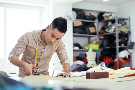 Young man working as a tailor and using scissors in his work in atelier, he making a new dressの写真素材