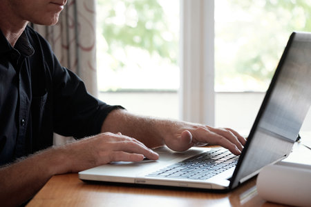 Close-up view of unrecognizable senior businessman working on laptop while sitting at office desk in...