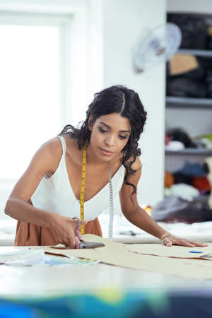Woman cutting fabric on sketch lines with scissors, preparing details of material for new dressの写真素材