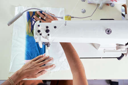 Close-up of female seamstress working with fabric using sewing machine at the tableの写真素材
