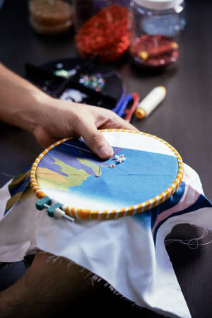 Close-up of man sewing a decorative colored beads on fabricの写真素材