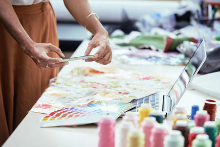 Close-up of female designer photographing colorful palette and textile lying on the table on her mobile phone for online conversationの写真素材