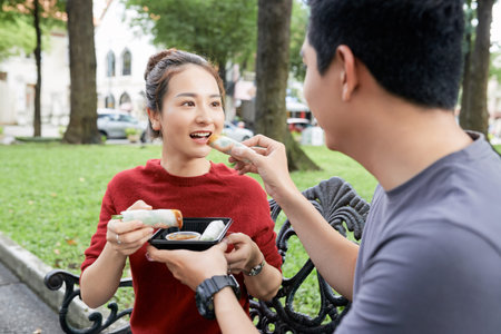Young Asian boyfriend and girlfriend feeding each other with spring rollsの写真素材
