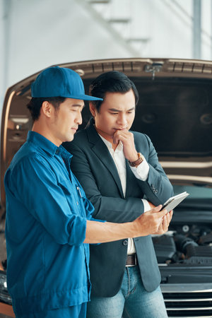 Auto technician showing the problem of car motor to the customer using digital tablet in workshop