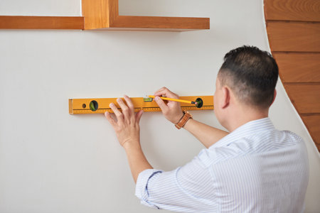Man doing repairment himself in the house, he checking the evenness of white wall using the level