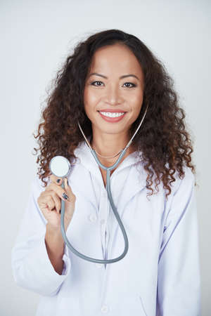 Portrait of young female doctor with curly hair holding stethoscope in front of the camera and smilingの写真素材
