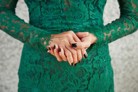 Close-up of woman standing in lacy green evening dress and has a beautiful manicure on her handsの写真素材