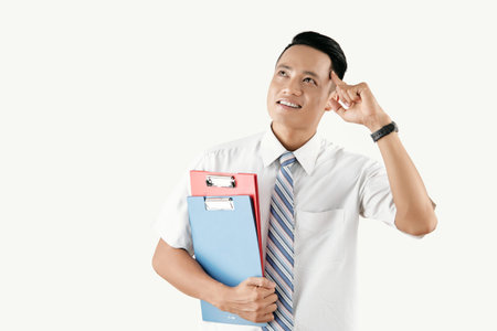 Young attractive Asian man holding forefinger near temple and smiling while pondering over creative...