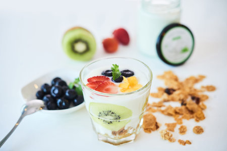 Composition of glass filled with yogurt and fruit on white table with granola and berries
