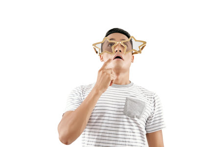 Waist-up portrait of young Asian man wearing funny star-shaped glasses grimacing and looking up...