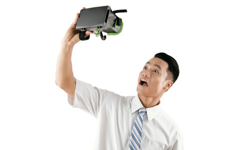 Young Asian male white collar worker making funny faces while playing with head-mounted display...