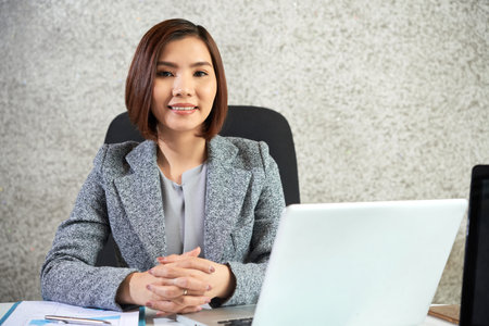 Portrait of confident female leader in jacket sitting at the table with laptop and smiling