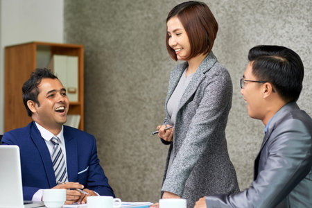 Smiling young female leader listening to her colleagues and they laughing together at the table...
