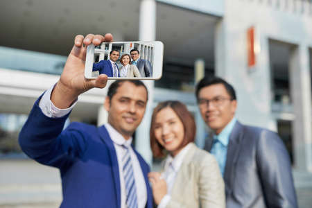 Businessman holding his smartphone and making selfie portrait together with his colleagues outdoorsの写真素材