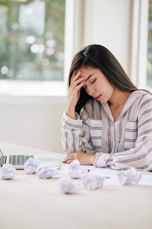 Modern beautiful Asian woman looking tired while working with papers and having problems with...