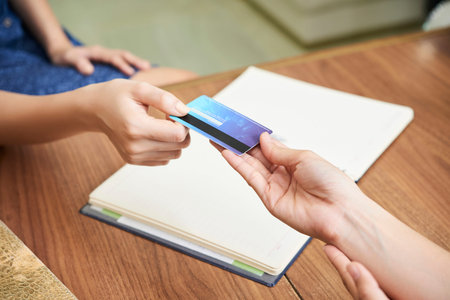 Crop shot from above of guest giving credit card to spa salon receptionist at counterの写真素材