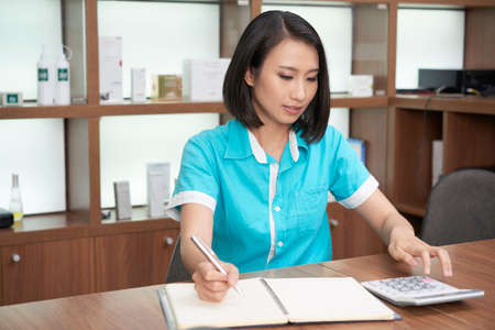 Pretty Asian woman working in spa salon and calculating while taking notes at working standの写真素材