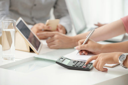 Crop shot of businesswoman using calculating machine and writing down numbers working with...