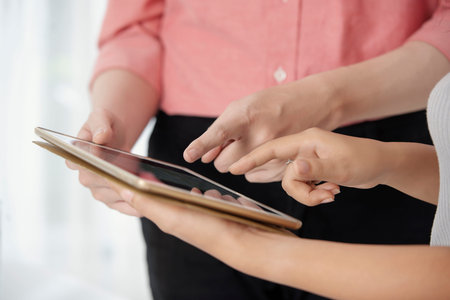 Faceless shot of modern young businesspeople sharing tablet while working in team