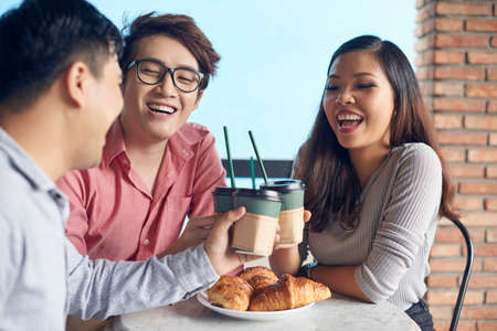 Young happy Asian woman and men toasting with coffee cup having fun on breakの写真素材