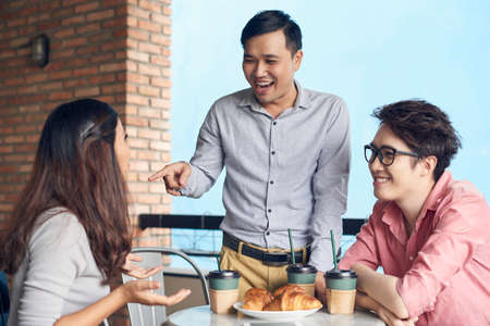 Contemporary young Asian men and woman having coffee break in cafeteria and having fun together while relaxingの写真素材