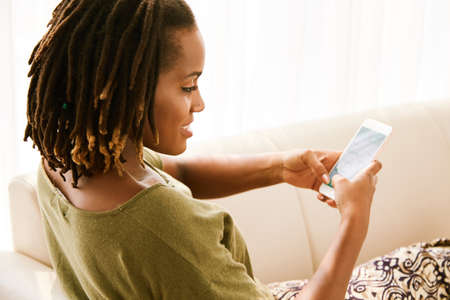 Pretty young woman resting on sofa and texting friendsの写真素材