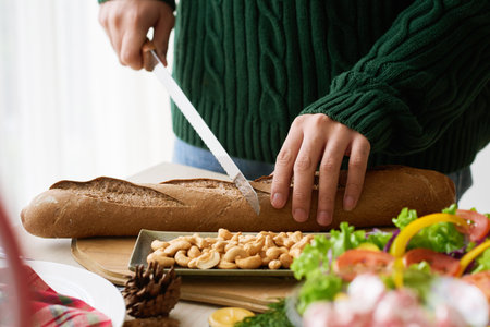 Close-up image of man cutting French baguette at dinner table