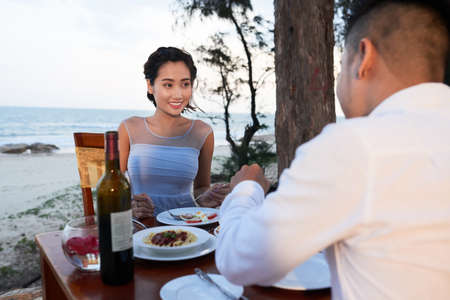 Beautiful attractive Vietnamese woman enjoying delicious foor and romantic dinner on beach with husbandの写真素材