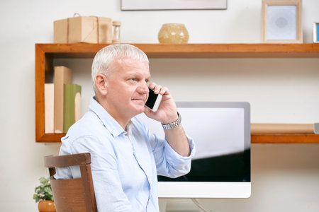 Serious mature entrepreneur sitting at office table and talking on phone