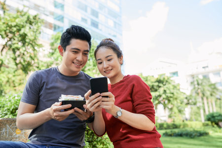 Happy young Asian couple posting photos of street food they made in park
