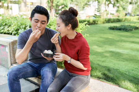 Young Asian couple enjoying delicious street food in park