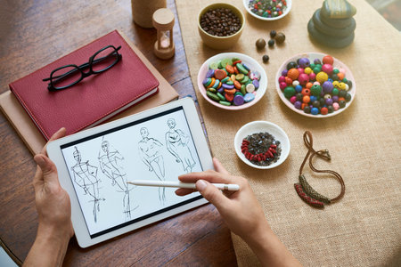 Close-up of female hands sitting at the table with plates with colorful beads and books and drawing...