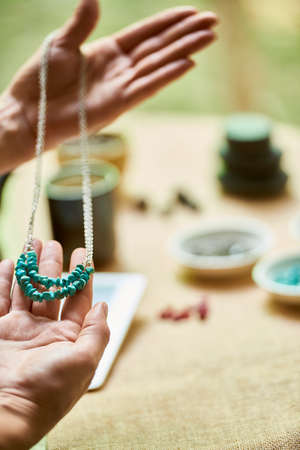 Close-up of woman holding finished handmade necklace on chain made from natural stonesの写真素材