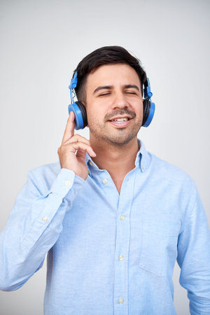 Portrait of young man enjoying music in his headphones and relaxing over white background