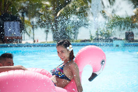 A loving couple in the pool on an inflatable pink flamingo having fun togetherの写真素材