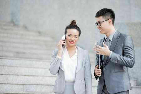 Smiling businesswoman talking on phone when her colleague is giving her adviceの写真素材