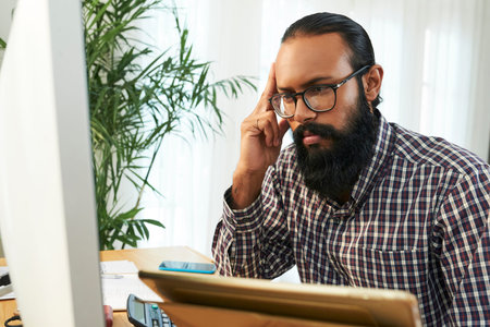 Bearded software developer in casualwear looking at coded data on computer screen and trying to read...