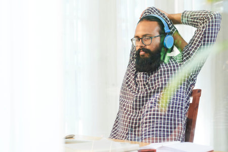 Young relaxed office worker doing physical exercise for arms while sitting by desk in front of computerの写真素材