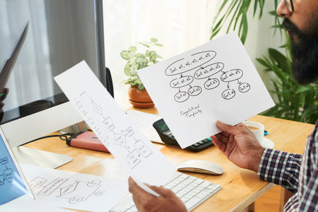 Programmer or software developer looking through papers with schemes containing information about...
