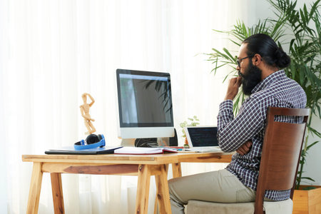 Modern programmer or it developer sitting by desk in front of computer screen and concentrating on...