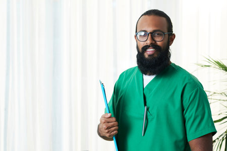 Portrait of bearded doctor in green uniform holding medical documents under his arm, copy space to...