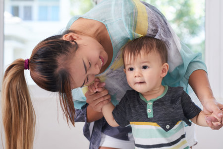 Smiling Asian woman dancing with her little son at home