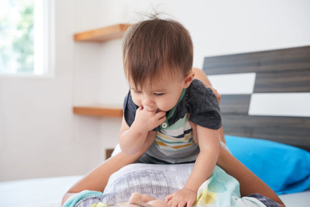 LIttle boy sucking his fingers when his his playing with mother at homeの写真素材