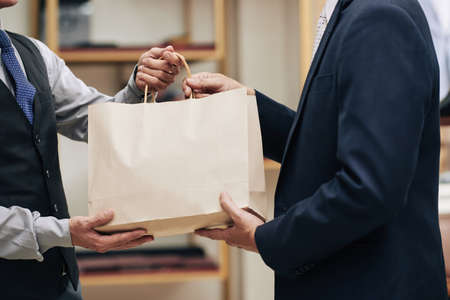 Shop assistant giving male customer paper-bag with his purchaseの写真素材