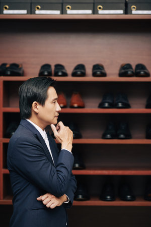Pensive mature man standing at shoe shelf in fashion boutiqueの写真素材