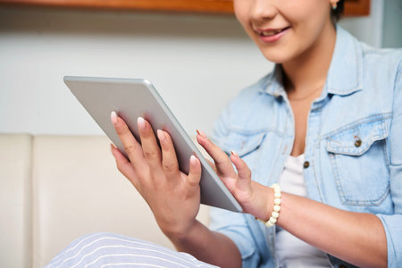 Young woman holding digital tablet and communicating online with her friends at home