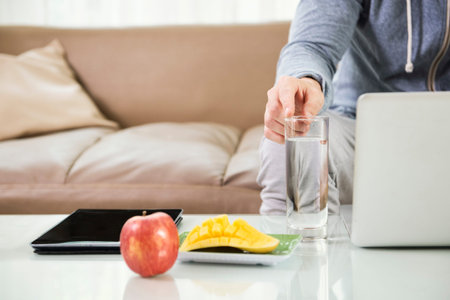 Close-up of fresh fruits and tablet pc on the table with man pointing at glass of water while using...