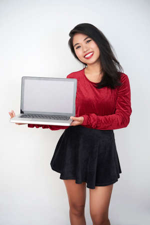 Portrait of Asian beautiful model standing and holding laptop and smiling at camera on white backgroundの写真素材