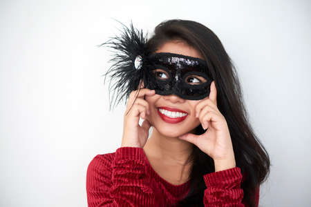 Portrait of beautiful young lady in black masquerade mask smiling on white backgroundの写真素材